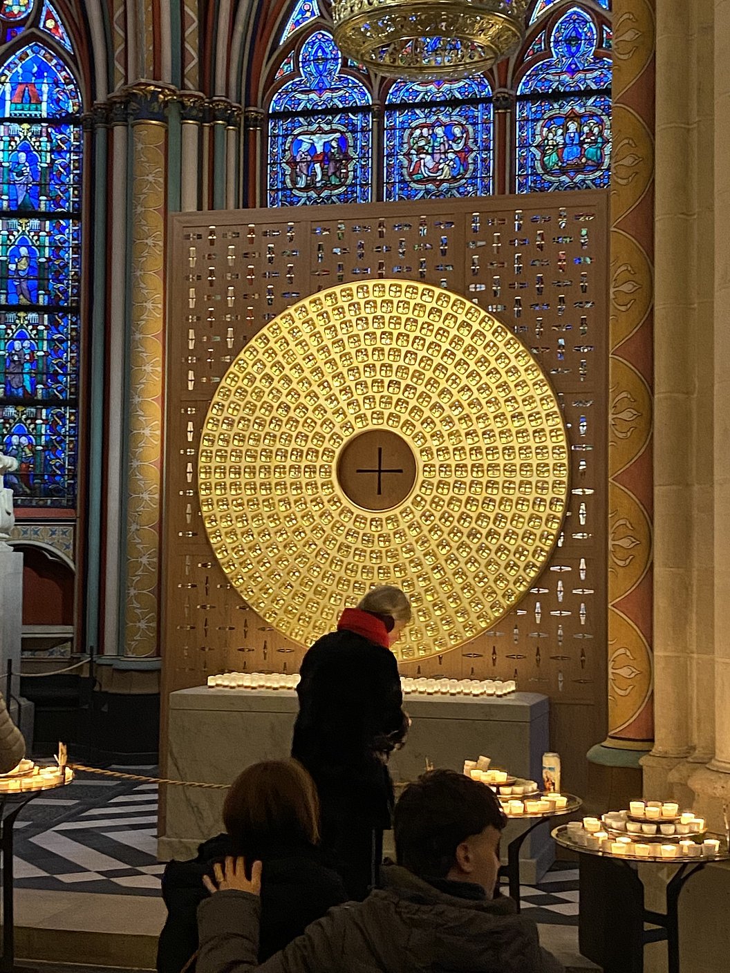 Person vor einer großen goldfarbenen runden Tafel mit vielen kleinen Symbolen in einer Kirche mit bunten Glasfenstern