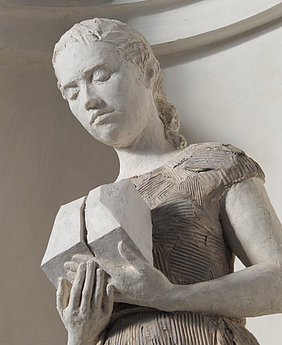 Skulptur einer Frau mit zusammengebundenem Haar, die zwei geometrische Formen in den Händen hält